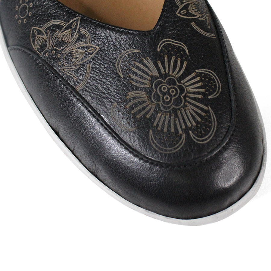 FRONT VIEW OF BLACK CASUAL SHOE WITH VELCRO STRAP AND WHITE SOLE. FLOWERS ON THE SIDES AND TOP OF THE SHOE 